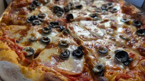 Lezzetli siyah zeytinlerle bezenmiş, peynirli, lezzetli bir pizzanın baştan çıkarıcı yakın çekimi, yemek severler için mükemmel.