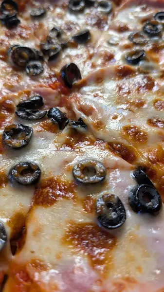 Yakından bakınca, eritilmiş peynirli pizzanın siyah zeytinlerle kaplı olduğunu görüyoruz. Her yerde yemek severler için ideal.