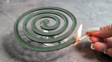 Yakındaki güzel desenli bir yüzey üzerinde duran yeşil sarmal bir sarmalı ateşlemek için bir kibrit çakıyor.