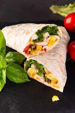 Kızarmış tavuk eti, sebze ve mısırla sarılmış tortilla. Koyu arkaplanda lezzetli kesilmiş burrito