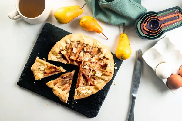Baked galette or open pie with pear, cinnamon and almond flakes on the table