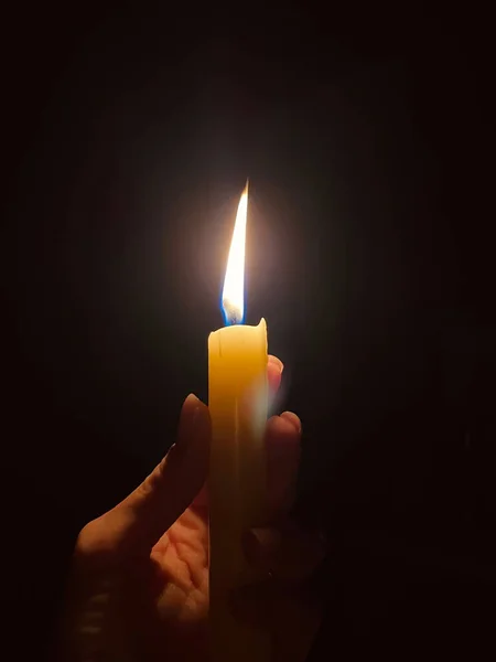 burning candle in the hands of a woman on a black background