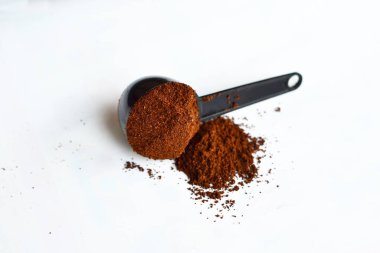 Siyah kaşıkta öğütülmüş kahve beyaz arka planda yatar.
