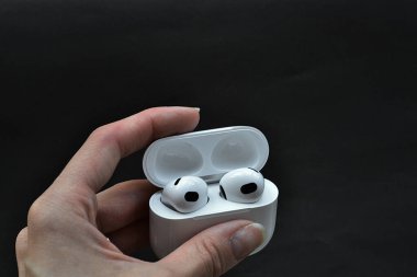 Kızın elinde beyaz kablosuz kulaklık var.