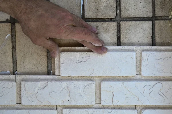 A man puts a light tile on the wall