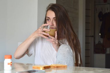 The girl sits at the table and drinks coffee