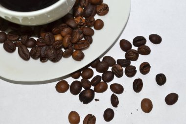 Kahve çekirdekleri bir fincan kahvenin yanına serpilmiş.