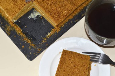 Siyah tabakta dilimlenmiş ballı kek ve bir fincan kahve.