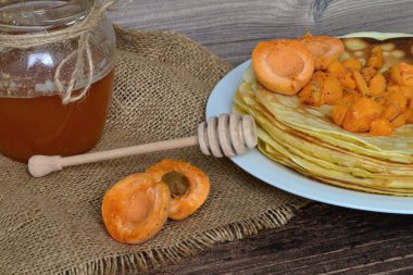 Masanın üzerinde bir tabak dolusu krep ve çuval bezinde kayısı var.