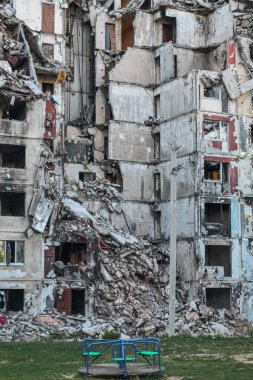 Yıkılmış bir gökdelenin yanında çocuk salıncağı.