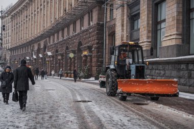 KYIV, UKRAine - 8 ARALIK 2023: BİR YAŞIK YAŞAĞI YAŞIYOR VE ŞEHRİMDEN ÇEKİYOR. Ve insanlar karları kürekle temizliyor. Traktör yolu temizliyor.
