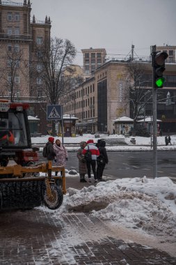 KYIV, UKRAine - 8 ARALIK 2023: BİR YAŞIK YAŞAĞI YAŞIYOR VE ŞEHRİMDEN ÇEKİYOR. Ve insanlar karları kürekle temizliyor. Traktör yolu temizliyor.