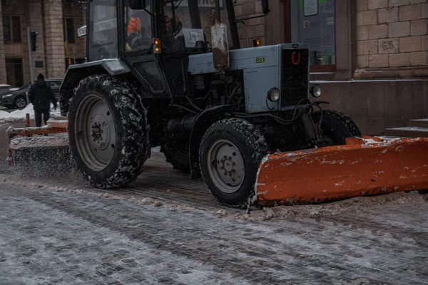 KYIV, UKRAine - 8 ARALIK 2023: BİR YAŞIK YAŞAĞI YAŞIYOR VE ŞEHRİMDEN ÇEKİYOR. Ve insanlar karları kürekle temizliyor. Traktör yolu temizliyor.