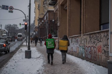 Kyiv, Ukrayna - 8 Aralık 2023: Sabahtan beri şehir kar altında. Farklı renkte portföyleri olan iki yemek dağıtıcısı var. Sokakta dondum.