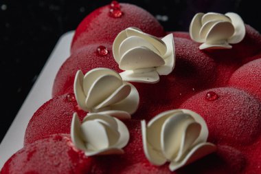 Kyiv, Ukrayna - 5 Şubat 2024 güzel mus, küçük toplar şeklinde kırmızı pasta. Üstünde beyaz çikolata çiçekleri var. Doğum günüm için bana pasta verdiler. Pasta siyah bir masanın üzerinde duruyor. lezzetli ahududu aromalı.