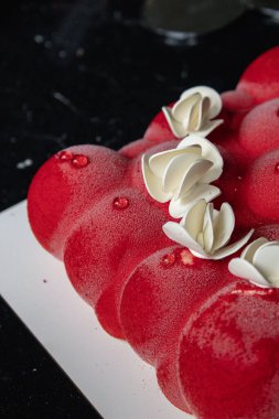 Kyiv, Ukrayna - 5 Şubat 2024 güzel mus, küçük toplar şeklinde kırmızı pasta. Üstünde beyaz çikolata çiçekleri var. Doğum günüm için bana pasta verdiler. Pasta siyah bir masanın üzerinde duruyor. lezzetli ahududu aromalı.