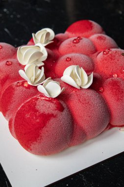 Kyiv, Ukrayna - 5 Şubat 2024 güzel mus, küçük toplar şeklinde kırmızı pasta. Üstünde beyaz çikolata çiçekleri var. Doğum günüm için bana pasta verdiler. Pasta siyah bir masanın üzerinde duruyor. lezzetli ahududu aromalı.