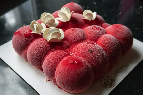 Kyiv, Ukraine - February 5, 2024. beautiful mousse, red cake in the shape of small balls. white chocolate flowers on top. they gave me a cake for my birthday. the cake lies on a black table. delicious raspberry flavor.