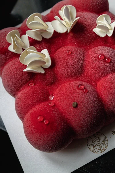 Kyiv, Ukraine - February 5, 2024. beautiful mousse, red cake in the shape of small balls. white chocolate flowers on top. they gave me a cake for my birthday. the cake lies on a black table. delicious raspberry flavor.