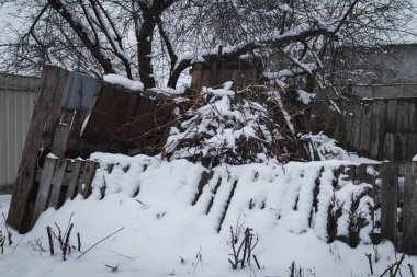 Kyiv, Ukrayna - 10 Şubat 2024. Büyükannemin köyünde karlı bir bahçe. Çatıdan sarkıtlar sarkıyor. Evin çatısında kar var. Sokakta karla kaplı kapalı bir kabuk. Kasvetli hava, gri gökyüzü