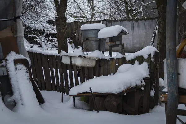Kyiv, Ukrayna - 10 Şubat 2024. Büyükannemin köyünde karlı bir bahçe. Çatıdan sarkıtlar sarkıyor. Evin çatısında kar var. Bahçede bir kuyu var. Kapalı, su yok.