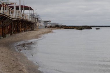 Odesa, Ukrayna. 20 Mart 2024, bulutlu bir günde, insanlar deniz kıyısında yürüyorlar ve birçok kuş uçuyor. Yakınlardaki güzel mimari.