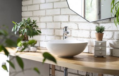 Ahşap tezgahta seramik lavabo ve beyaz tuğla duvarda ayna olan modern banyonun şık iç tasarımı..