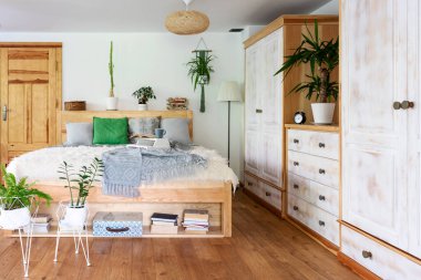 Yatak odasının içinde yastıklı çift kişilik yatak odası ve otelde boho tarzında yatak örtüsü. Odanın içinde doğal ahşap ahşap, ahşap mobilyalar, gardırop, çekmeceler ve zemin. Bitkilerle ve şık dekorlarla dolu rahat bir ev..