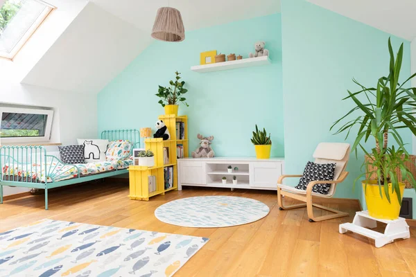 Cozy interior of room child with pastel color on the wall and yellow color in decor. Room in the attic with bed, armchair and carpet in modern design. Scandinavian concept.