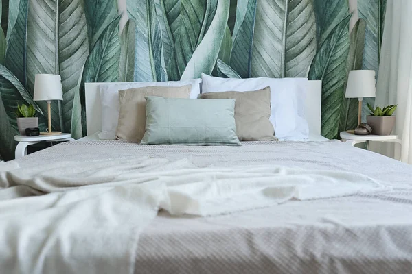 stock image Bedrrom in cozy interior with modern design. Bed with pillows and green leaves on a wallpaper on the wall.