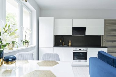 Yeni beyaz mutfak mobilyaları, masa ve sandalyelerle stüdyo dairesinin içinde. Penceresi ve modern tasarımı olan oda.