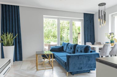 Deniz mavisi rahat kanepe, pencereli oturma odasının yeni iç kısmında. Modern dekorlu bir dairede oturma odası..