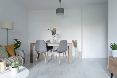 Modern iç mekanlarda masa ve sandalyelerle dolu bir oturma odası. Beyaz duvarı, kanepesi ve ahşap zemini olan şık bir daire..