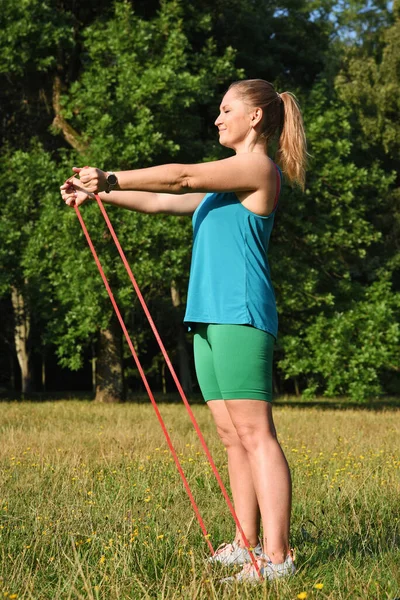 Stretching exercise with rubber band outdoor. Active woman in sportswear training sport and fitness in a park. Vertical