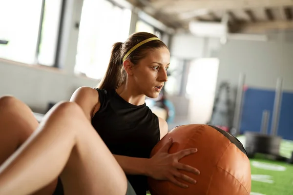 Fitness woman make physical exercise and functional training with ball in a gym with another people. Sporty girl during cross fit. Indoors.