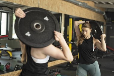 Spor giyim eğitiminde spor salonunda spor salonunda halter diski olan kaslı bir kadın. Spor, vücut geliştirme, güç kavramı. Dişi yaya geçidi.
