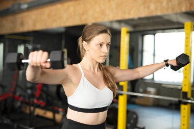 Spor salonunda dambıllarla antrenman yapmak. Spor salonundaki kadın egzersizleri. Kapalı alanda vücut geliştirme.