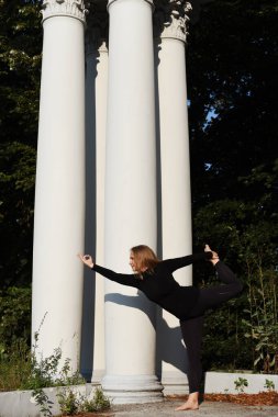 Yoga pozisyonunda duran bir kadın, parkta meditasyon ve vücut dengesi yapıyor. Dans ve mutluluk. Dikey. Sağlıklı yaşam tarzı.