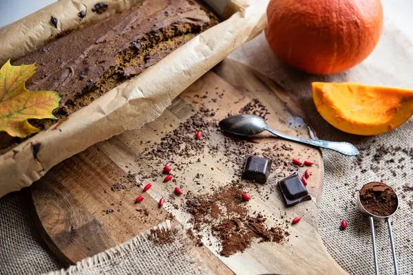 Pumpkin cake with chocolate as a sweet healthy dessert on wooden board with spoon. Autumn in the kitchen with leaf. Food for halloween. Closeup.