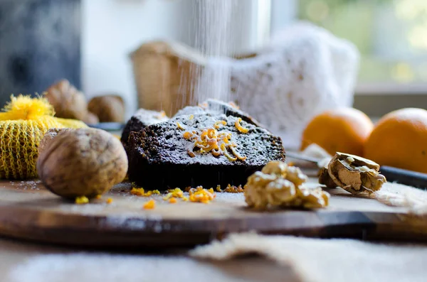 Christmas black cake with nuts, orange peel and sugar on the wooden board. Christmas mood. Close up.