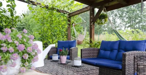 Covered terrace with rattan furniture, flowers, hammock, green nature and flowers. Outdoor veranda with sofa, table and chairs. Beautiful place for relax in garden.Banner panoramic.