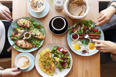 Kahvaltı için farklı renkte yemekler ya da kadın eli çatal bıçaklı bir tabakta öğle yemeği zamanı. Lokantada sahanda yumurta, omlet, bruschetta ve sosis. Düz üst görünüm.