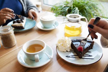 Sabah kafede kadınların toplantısı sırasında bir fincan çayla çikolatalı kek. Çatal tutan bir kadın. Kapat..