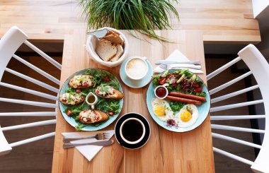 Kahvaltı için farklı rengarenk yemekler ya da sofrada çatal bıçak takımı olan bir tabakta öğle yemeği zamanı. Restoranda kızarmış yumurta, omlet, bruschetta ve bir fincan kahveyle sosis. Düz üst görünüm.