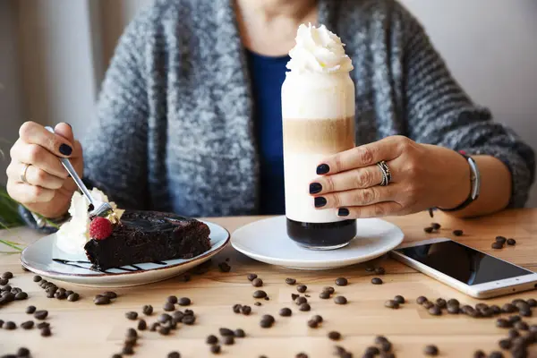 Woman eating chocolate cake brownie and drink coffee latte in restaurant. Relax time in the morning with delicious dessert and glass of coffee. Close up