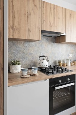 Mutfak mobilyaları, ahşap dolaplar ve duvarda desenli fayanslar ve üzerinde gaz ve su ısıtıcısı olan soba. Mutfağın modern iç mimarisi. Dikey.