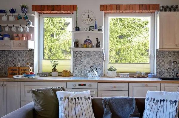 Interior of kitchen with view from window on forest, white wooden furniture and bricks as a decoration. Scandinavian style in a cottage with countertop and plant.
