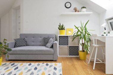 Çatı katında pencereli modern tasarım çocuk odası. Sandalyeli bir masa ve çocuklar için sarı desenli bir kanepe. Ahşap zeminde halı. İskandinav tarzı.