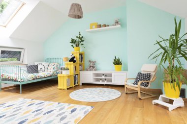 Tavan arasında penceresi olan bir oda çocuğu, ahşap zeminde modern tasarım halı, pastel duvar ve sarı mobilya. Yatağı, kitaplığı ve bitkisi olan çocuklar için rahat bir yer..