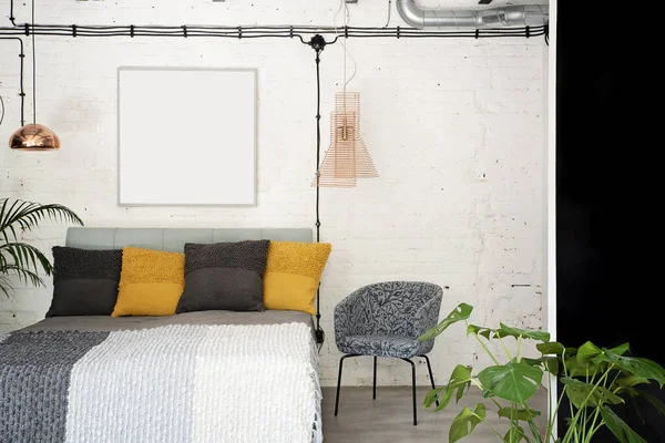 Industrial interior of loft apartment. Bedroom with double bed with pillows and brick wall with blank frame with mock up. Scandinavian style.